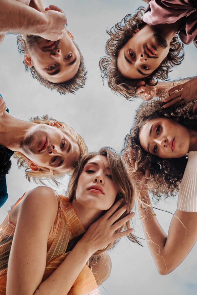 CentreSalons_Denver-23 Five people with varied hairstyles and facial expressions stand in a circle, looking down toward the camera against a light sky background.