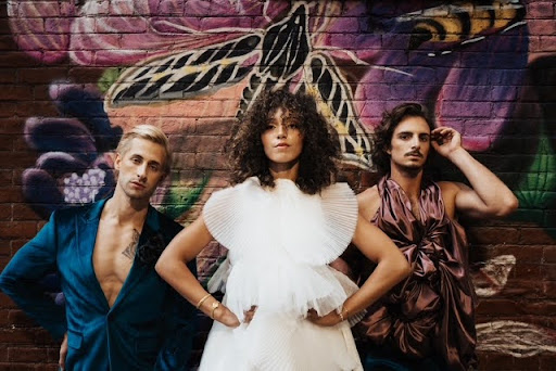 Person with a chin-length bob haircut in platinum blonde, hair covering one eye, wearing a black asymmetrical dress, stands against a dark background—capturing an edgy spring vibe.