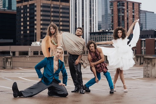 Person with a chin-length bob haircut in platinum blonde, hair covering one eye, wearing a black asymmetrical dress, stands against a dark background—capturing an edgy spring vibe.