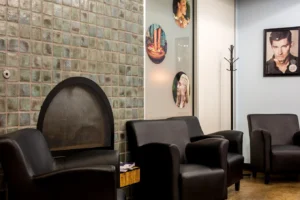 centresalon-arvada-23 A waiting area with black armchairs, a tiled wall, circular images of hairstyles, a framed portrait, and a coat rack.