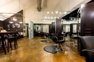 centresalon-arvada-30 Modern hair salon interior with empty black styling chairs, large mirrors, wooden stations, and wall art under bright lighting.