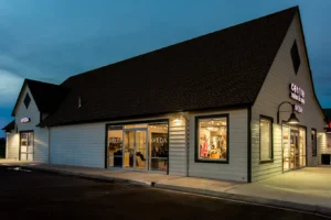 centresalon-arvada-42 A modern commercial building at dusk with large windows displaying products and illuminated signs reading "AVEDA" and "CARONA.