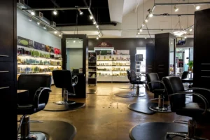 centresalon-arvada-53 Interior of a modern hair salon with empty black styling chairs, mirrors, and shelves stocked with hair products under bright lighting.