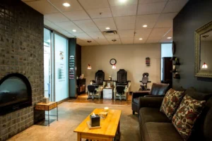 centresalon-arvada-68 A cozy nail salon interior with two pedicure chairs, a massage chair, a sofa with patterned pillows, a coffee table, and a fireplace. Shelves display nail polish bottles on the walls.